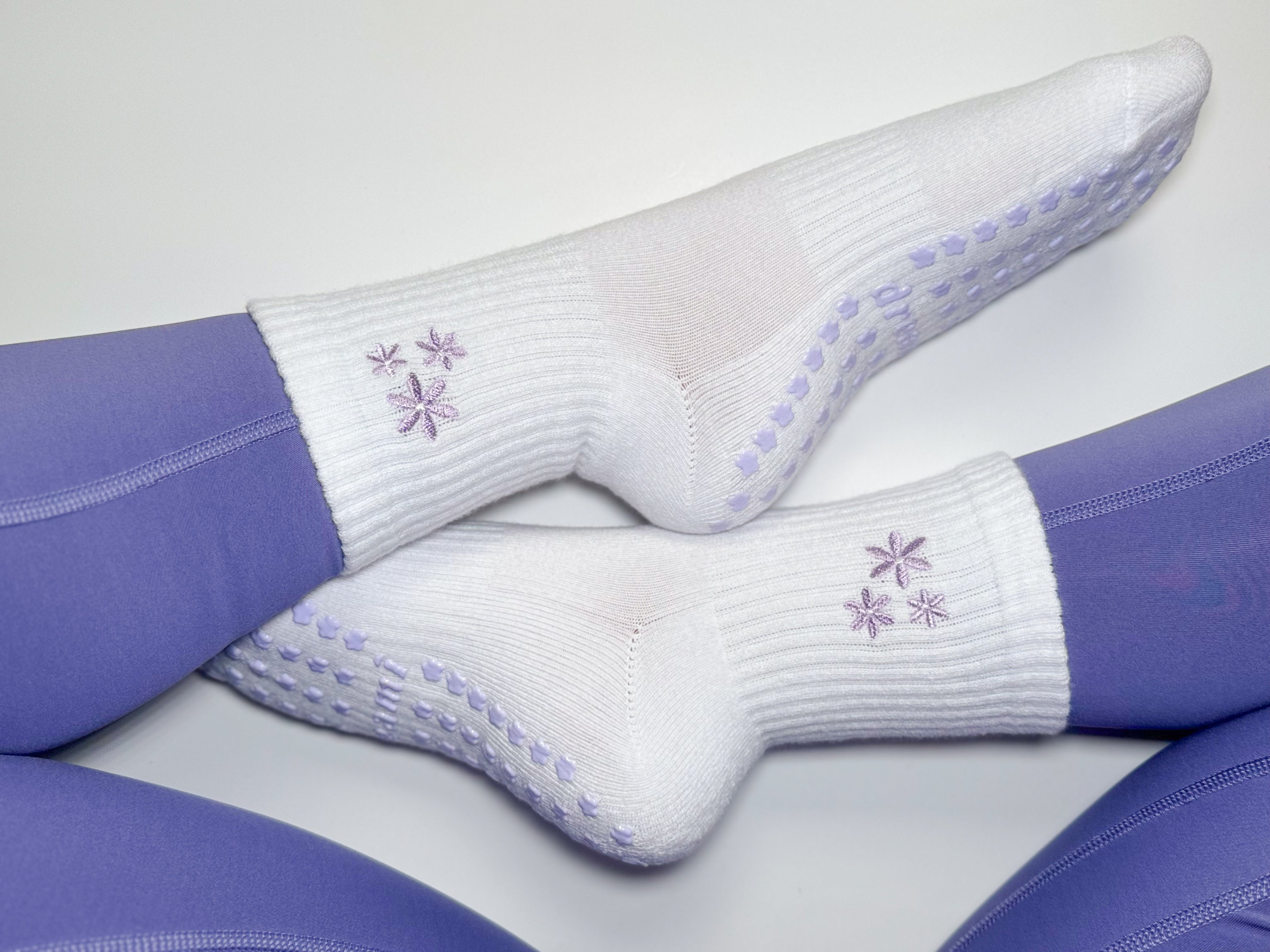 White socks with purple flower design and grips on person wearing purple leggings