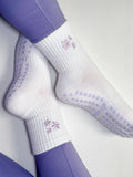 White socks with purple flower design and grips on person wearing purple leggings