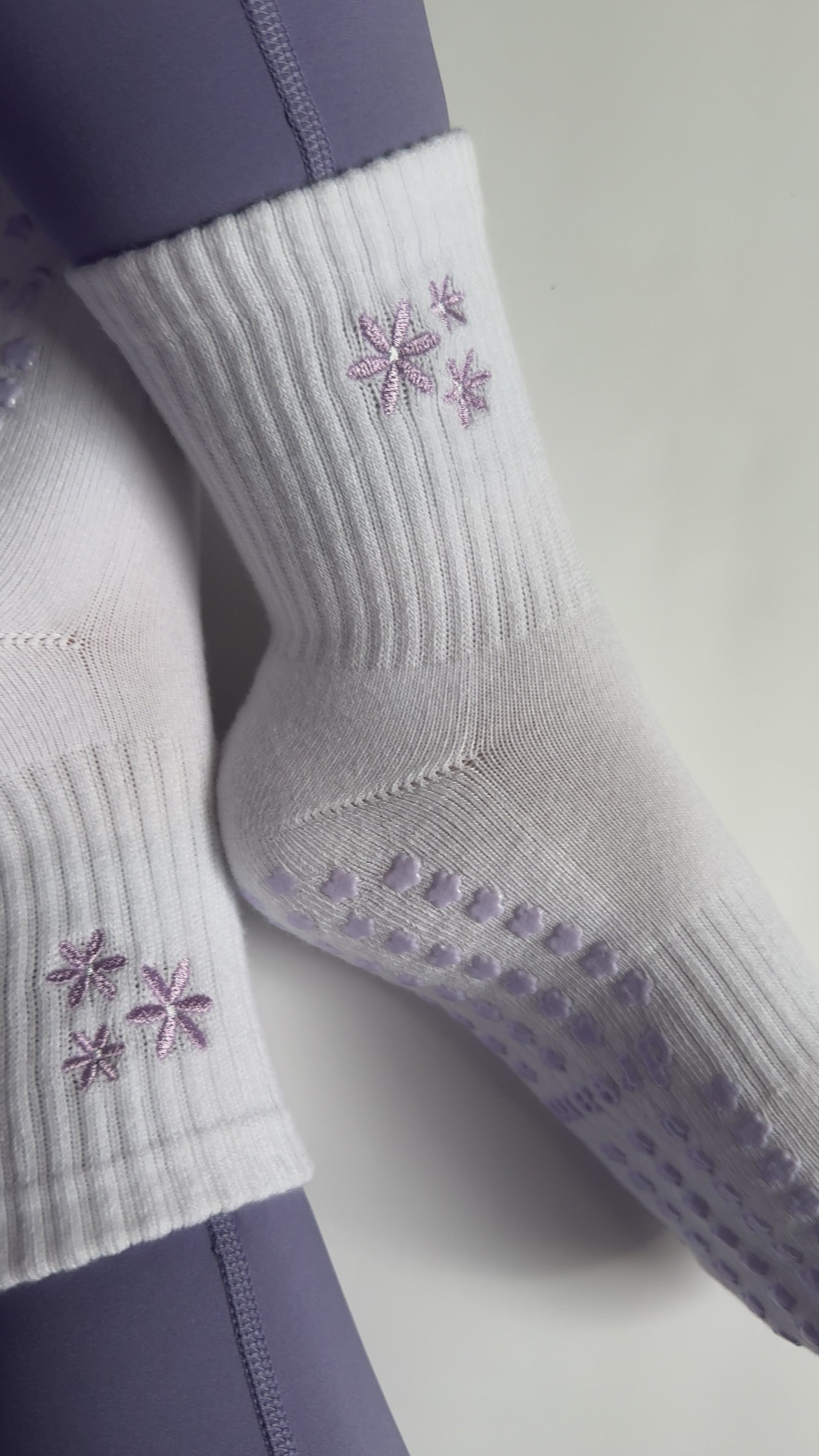 Video of white socks with purple flower design and grips on person wearing purple leggings